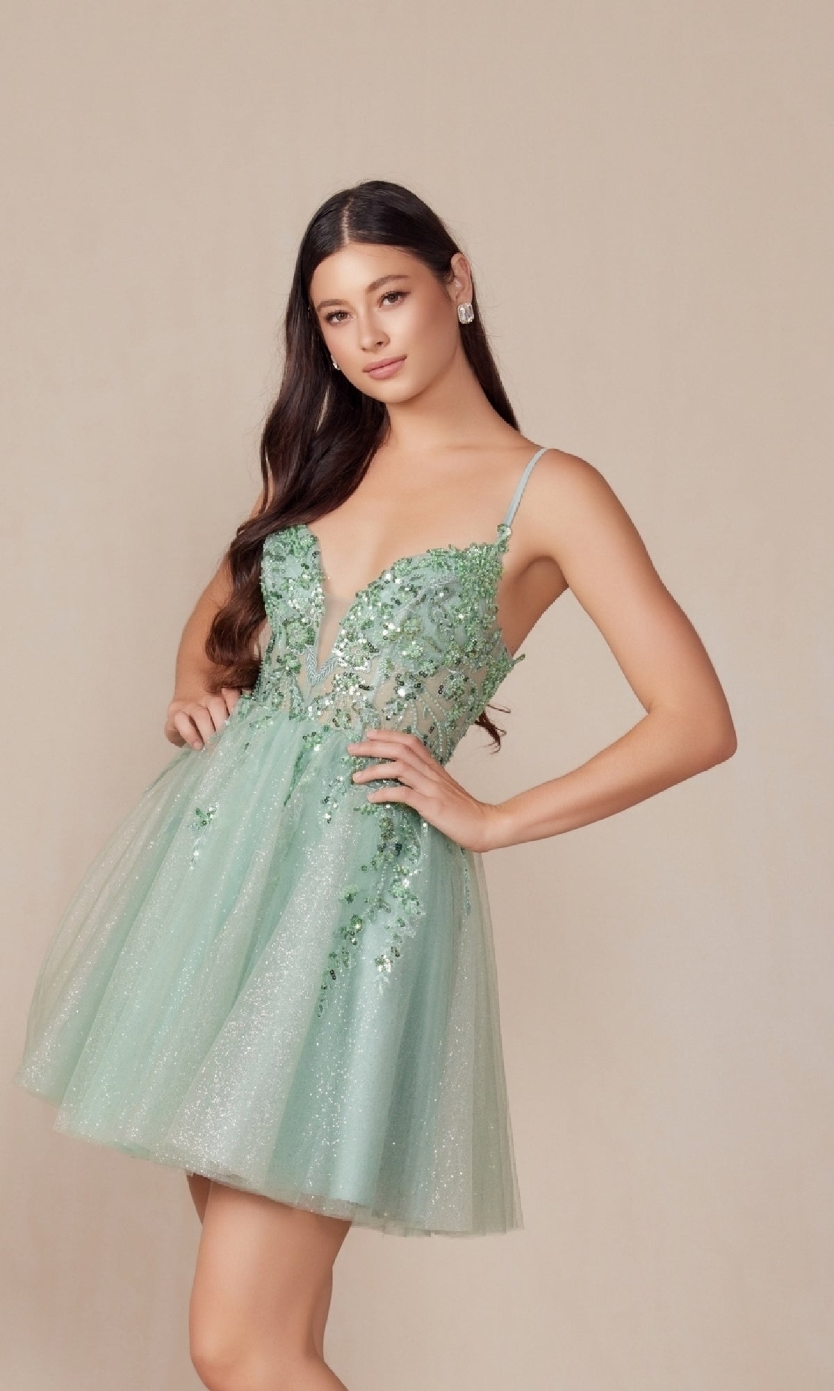 A woman models the Nox Anabel E902 Glitter Tulle Homecoming Dress, a light green, sleeveless V-neck style with sequin floral embroidery and a glittery tulle skirt against a plain background.